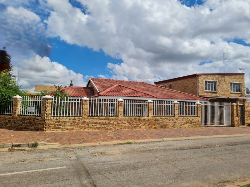 A well-maintained face brick house featuring a tiled roof, secure perimeter wall with steel fencing, and a paved driveway entrance.