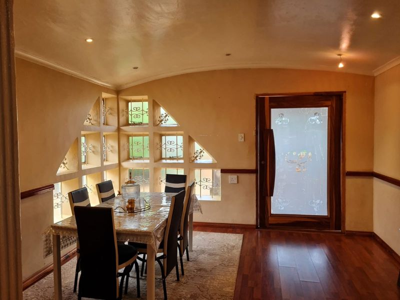 A dining room featuring unique geometric window cutouts with security grilles, timber flooring, and a decorative frosted glass entrance door.