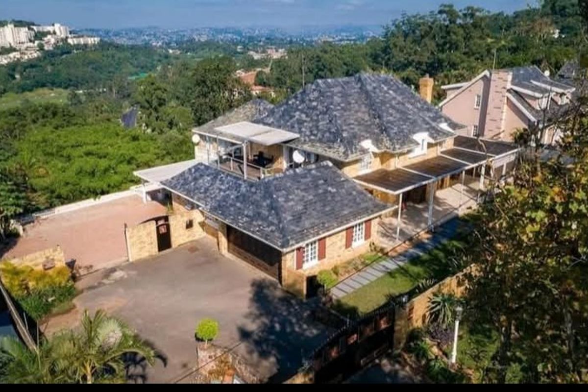Aerial view of a multi-level residential property featuring a slate roof, paved driveway, garage, and extensive covered patio areas set in a landscaped environment.
