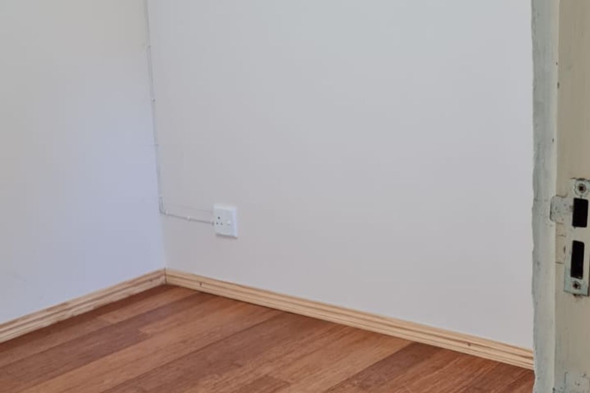 A clean, empty bedroom featuring warm-toned laminate flooring and neutral walls, providing a versatile blank canvas for interior design.
