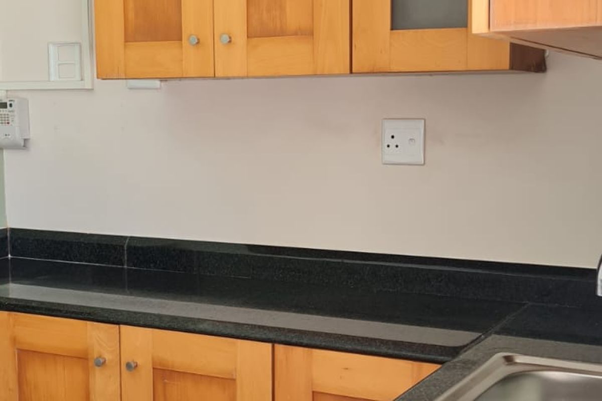 A functional kitchen area featuring wooden cabinetry, dark granite countertops, and a stainless steel sink, offering a practical layout for culinary tasks.