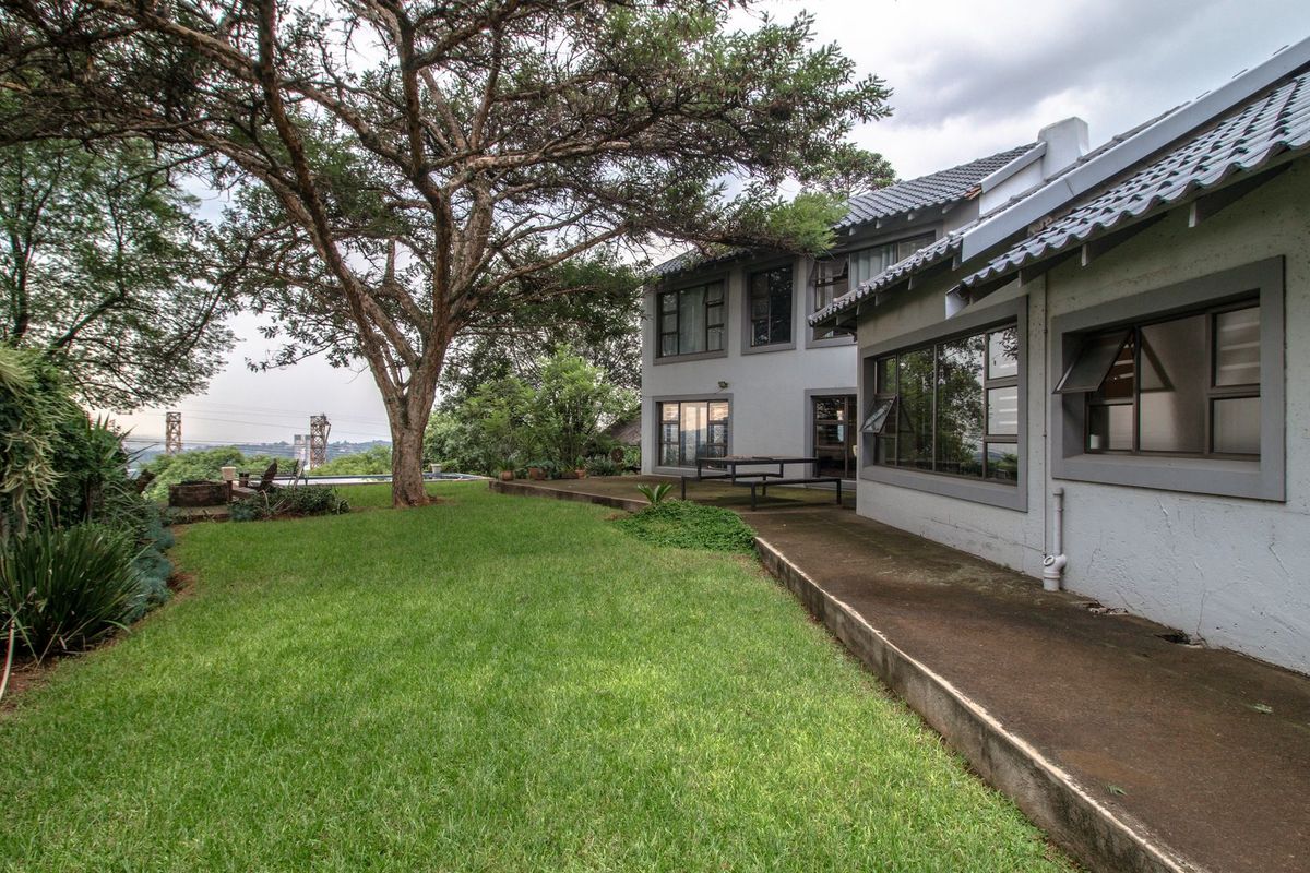 Rear view of the property featuring a spacious lawn, mature tree, and a concrete patio area adjacent to the main building structure.
