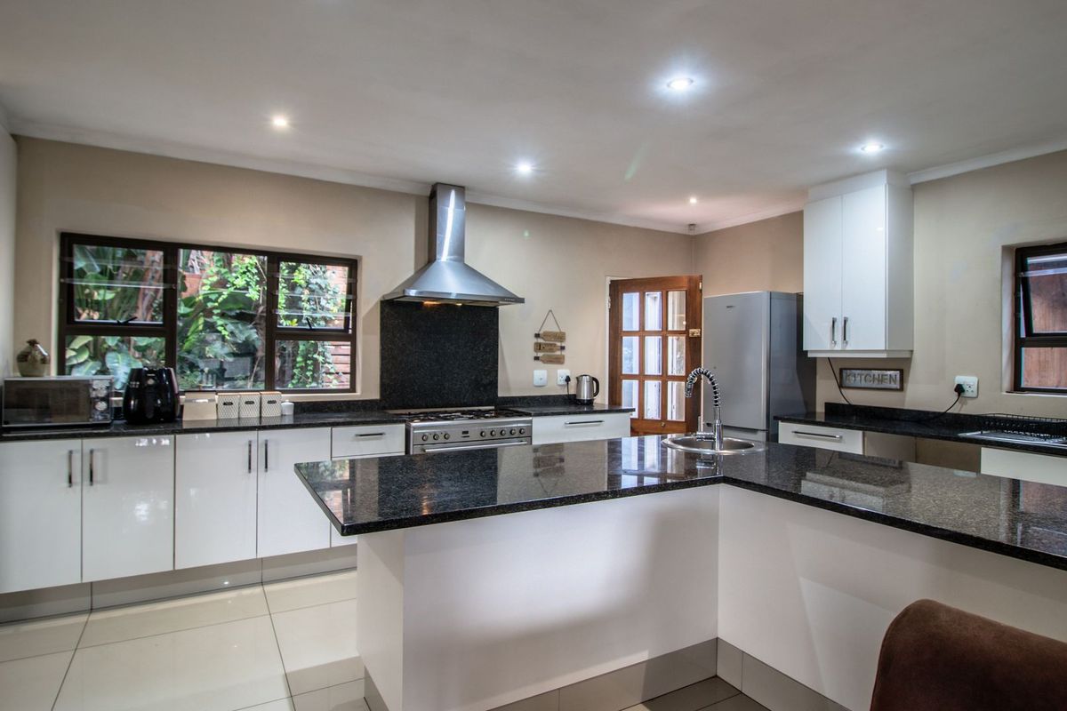 Modern kitchen featuring white cabinetry, dark granite countertops, a gas hob with stainless steel extractor, and tiled flooring with ample natural light.