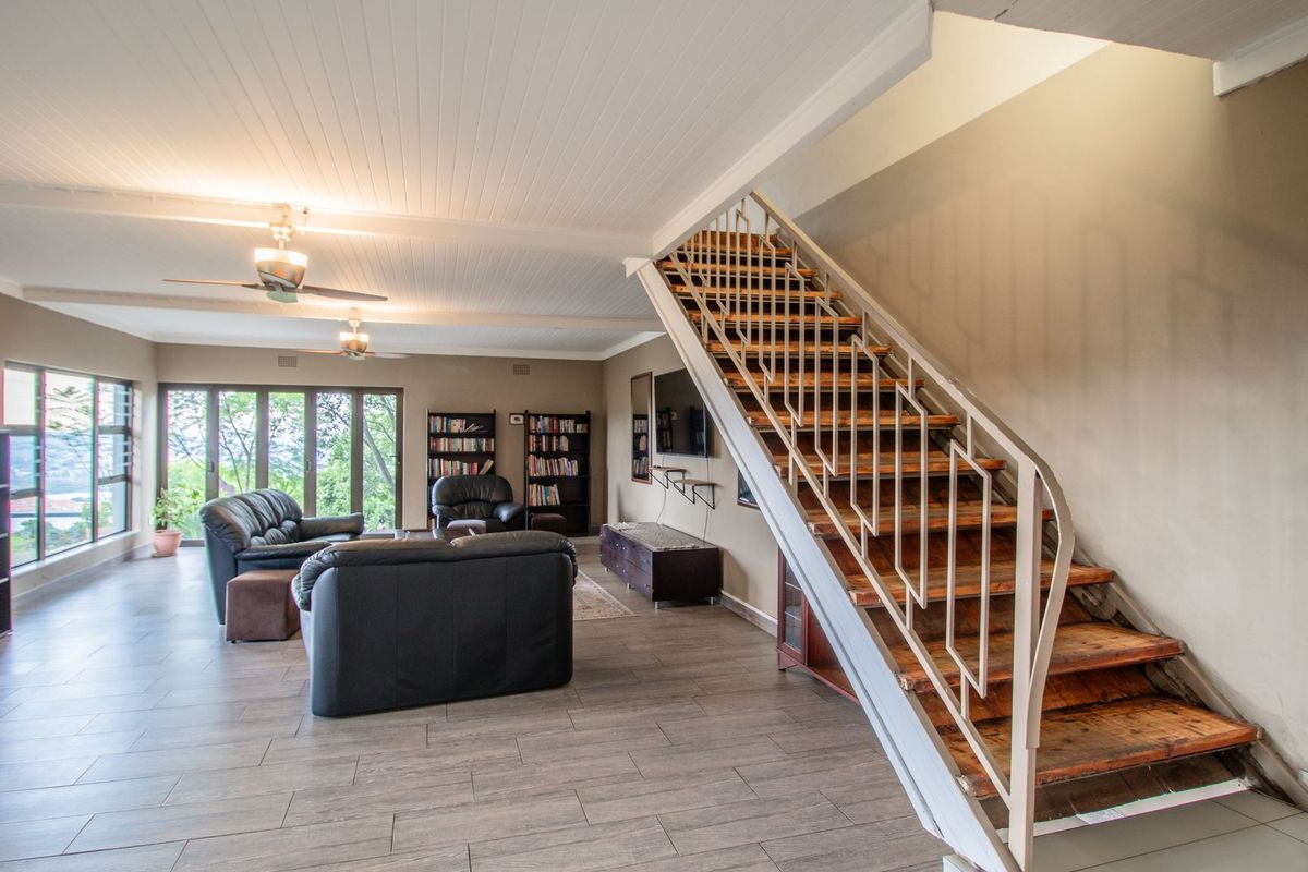 Spacious living area featuring a timber staircase with metal balustrade, tiled flooring, ceiling fans, and large sliding glass doors leading to an outdoor view.
