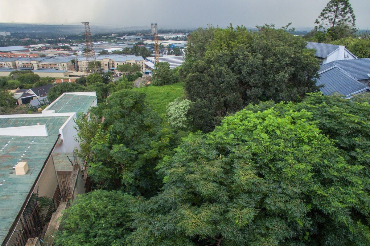 An elevated aerial view overlooking the property's roofline, surrounding mature trees, and the neighboring residential and industrial landscape.
