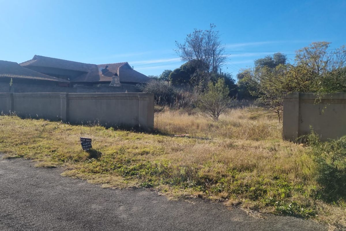 A vacant residential plot featuring a perimeter wall and direct street access, currently covered in overgrown grass and vegetation.