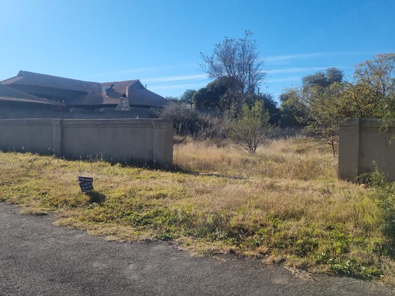A vacant residential plot featuring a perimeter wall and direct street access, currently covered in overgrown grass and vegetation.