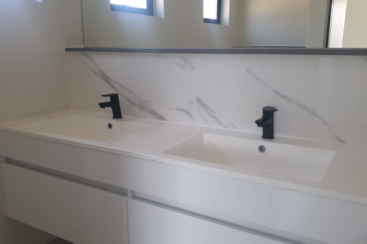 Modern bathroom vanity featuring a double sink setup, sleek black fixtures, and a marble-look splashback with a large integrated mirror.