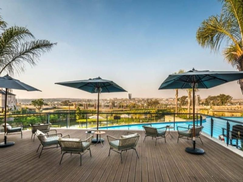 An elevated outdoor deck area featuring modern composite decking, metal safety railings, and a view overlooking a swimming pool and landscaped grounds.