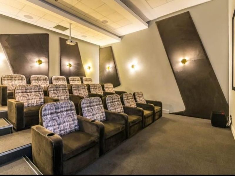 A dedicated cinema room featuring tiered seating, professional projection equipment, a large screen, and acoustic wall treatments for an immersive viewing experience.