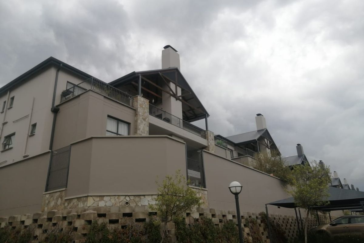 Exterior view of the apartment complex featuring stone cladding, metal roofing, and private balconies under a cloudy sky.