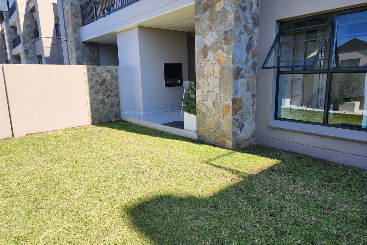 A well-maintained rear garden featuring a covered patio with a built-in braai, stone-clad pillars, and a neat lawn area.