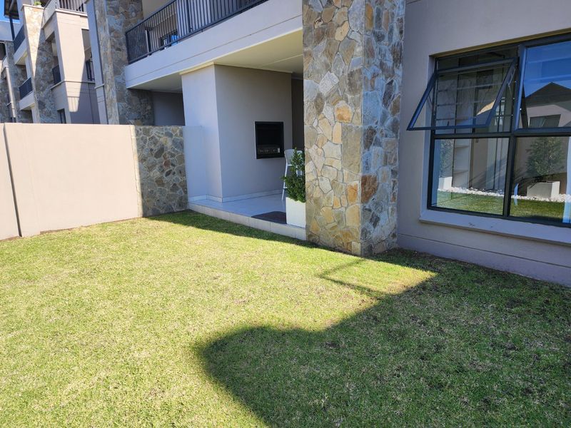 A well-maintained rear garden featuring a covered patio with a built-in braai, stone-clad pillars, and a neat lawn area.