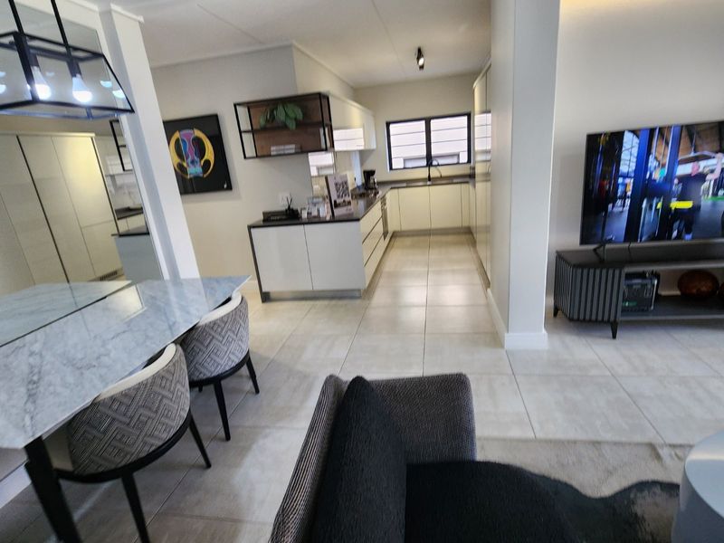 Modern open-plan living area featuring a sleek kitchen with built-in cabinetry, tiled flooring, and integrated lighting, seamlessly connecting to the dining and lounge space.