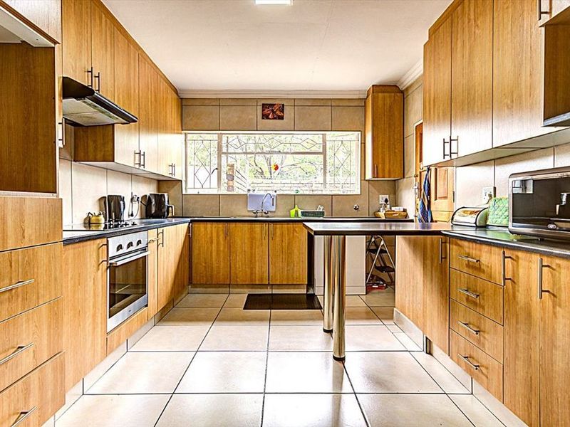 A functional kitchen featuring wood-look cabinetry, laminate countertops, a built-in oven, extractor fan, and tiled flooring with a breakfast bar area.