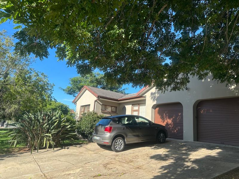 Front elevation of a residential house featuring a double garage, concrete driveway, and established garden under mature trees.