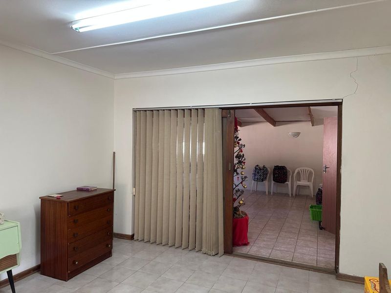 Living area featuring tiled flooring, vertical blinds, and a sliding door leading to an adjacent room, with a visible structural crack above the door frame.