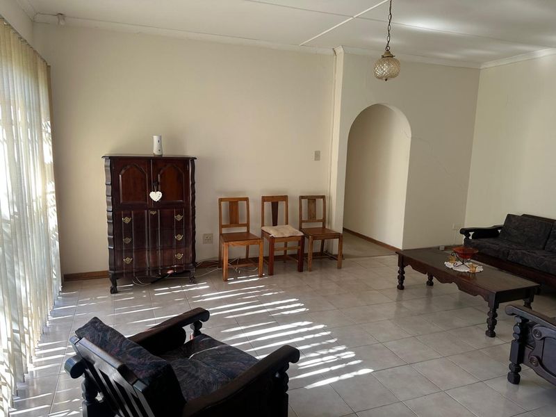 Spacious living room featuring tiled flooring, an arched entryway, and natural light through vertical blinds, requiring minor cosmetic attention to the wall.