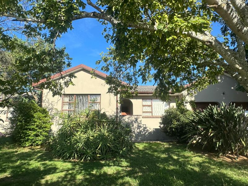 Front elevation of a single-story house featuring a tiled roof, plastered exterior walls, and security bars on the windows, set within a landscaped garden.