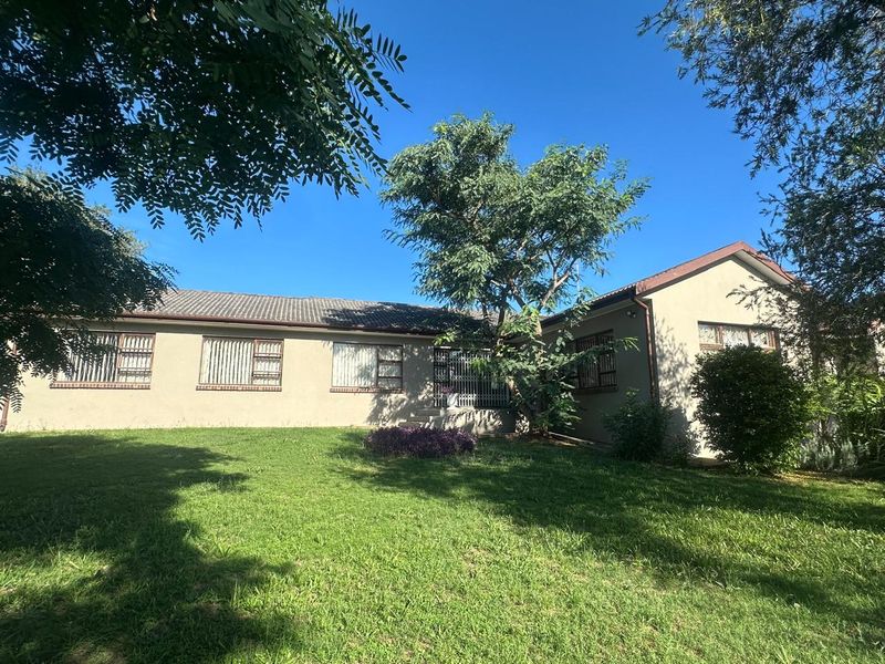 A view of the rear elevation of the house featuring a tiled roof, security bars on windows, and a spacious lawn area.