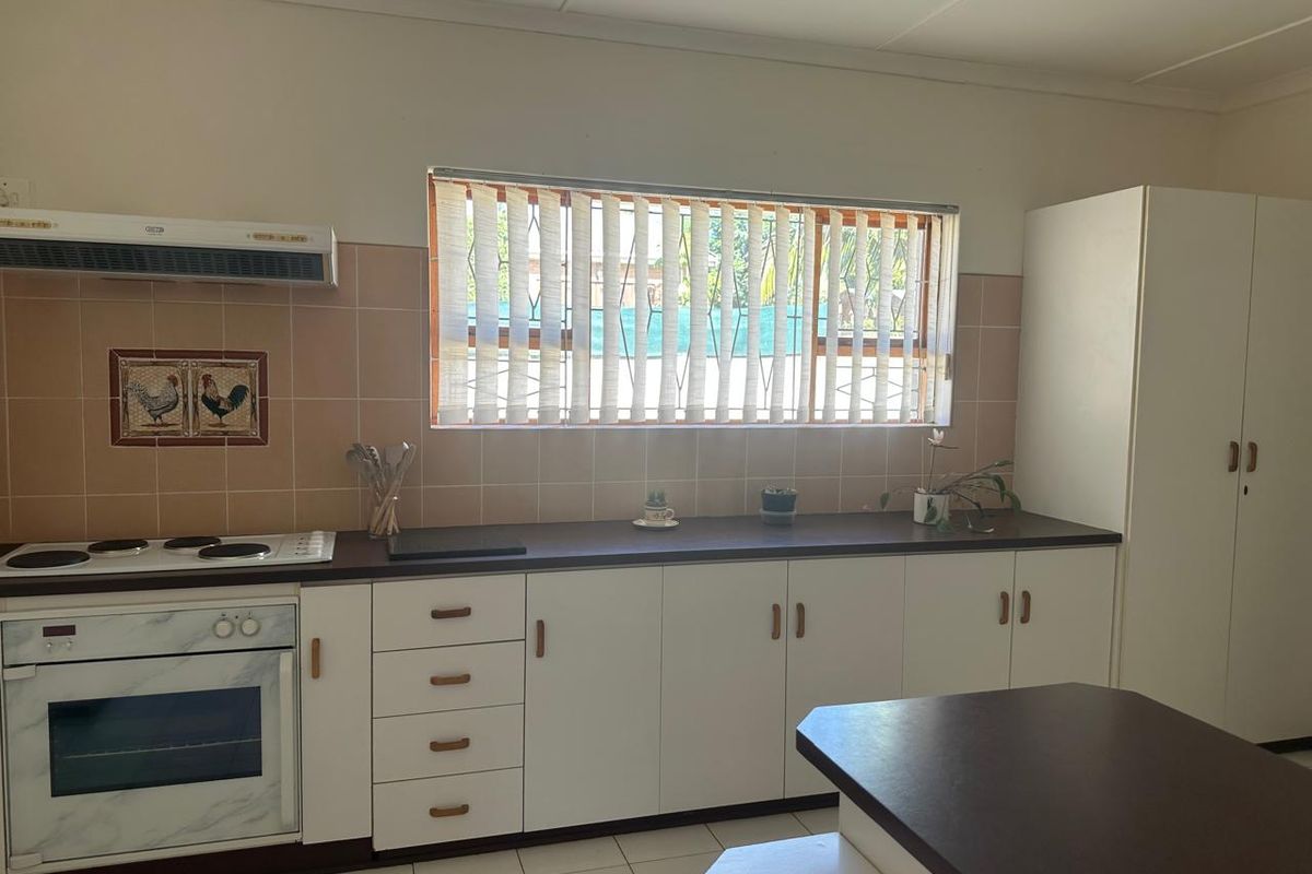 A functional kitchen featuring built-in cabinetry, an electric oven and hob, tiled backsplash, and ample counter space with vertical blinds over the window.