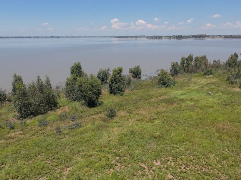 An aerial view of a vacant residential plot featuring natural vegetation and direct waterfront access.