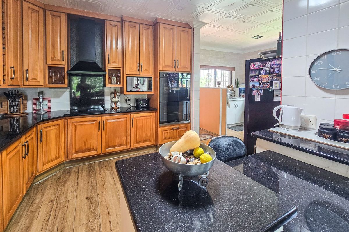 A functional kitchen featuring warm wooden cabinetry, black granite countertops, built-in oven, and decorative ceiling tiles, with an open flow to the adjacent area.