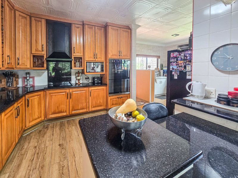 A functional kitchen featuring warm wooden cabinetry, black granite countertops, built-in oven, and decorative ceiling tiles, with an open flow to the adjacent area.