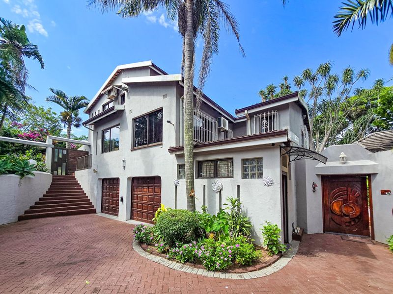 A multi-level residential property featuring a paved driveway, double garage, landscaped garden, and a distinctive timber entrance door.