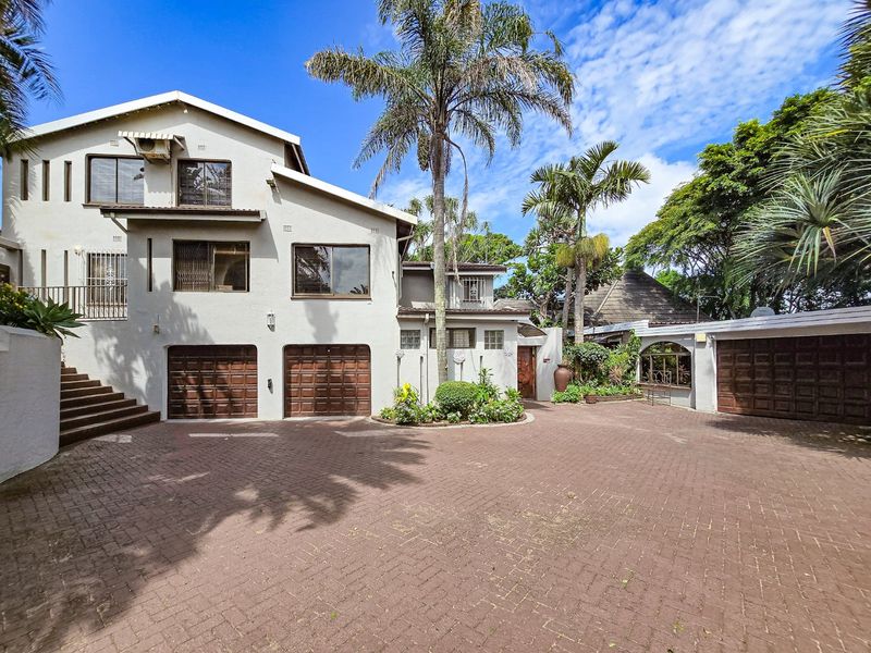 Front elevation of a multi-level house featuring a large paved driveway, multiple garage bays, and established garden landscaping.