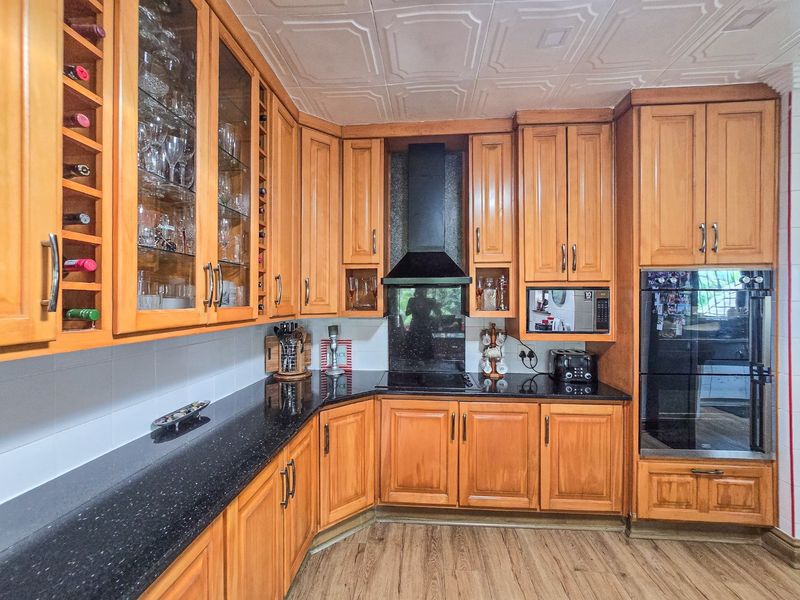 A functional kitchen featuring warm wooden cabinetry, black granite countertops, integrated appliances, and a distinctive coffered ceiling.