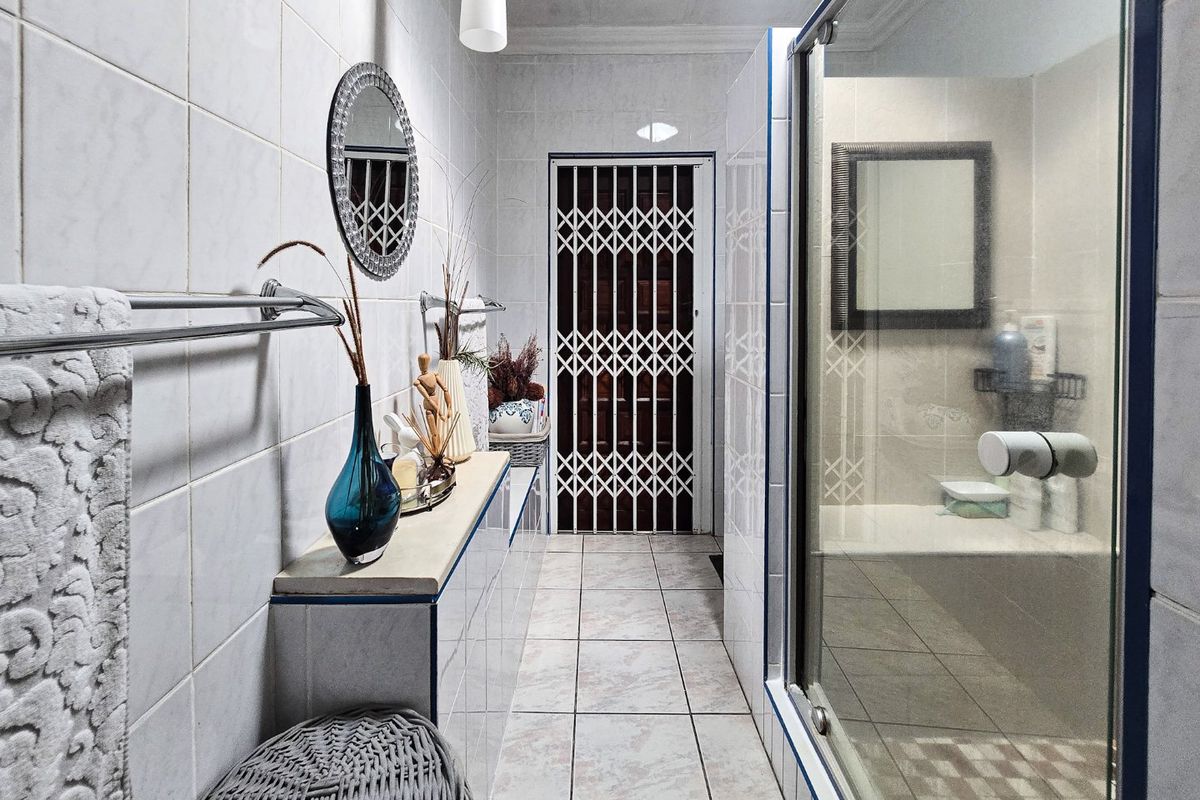 A functional bathroom featuring tiled walls and flooring, a glass shower enclosure, and a secure metal gate at the entrance.