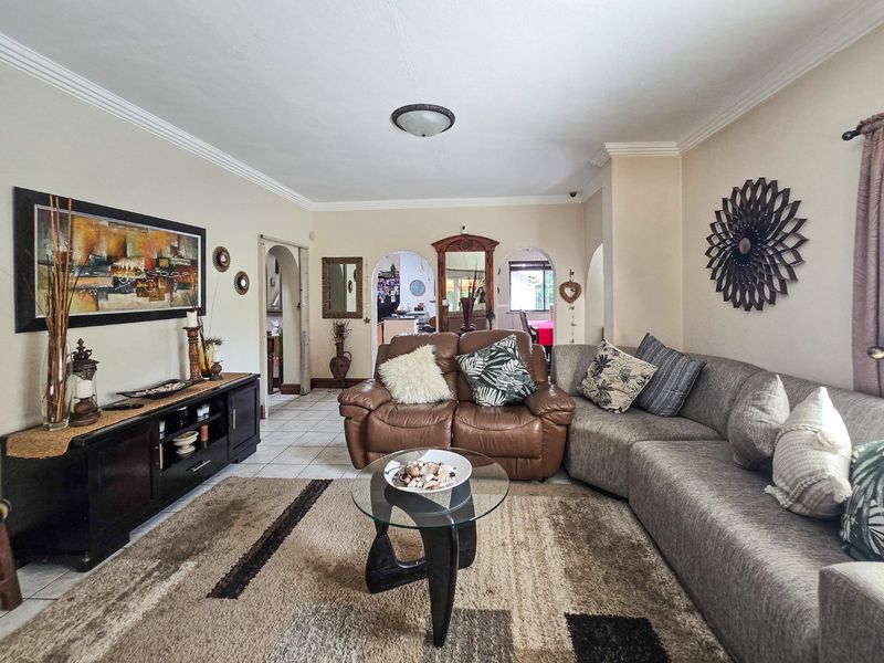 A spacious living room featuring tiled flooring, crown molding, and distinctive arched doorways leading to adjacent areas of the home.