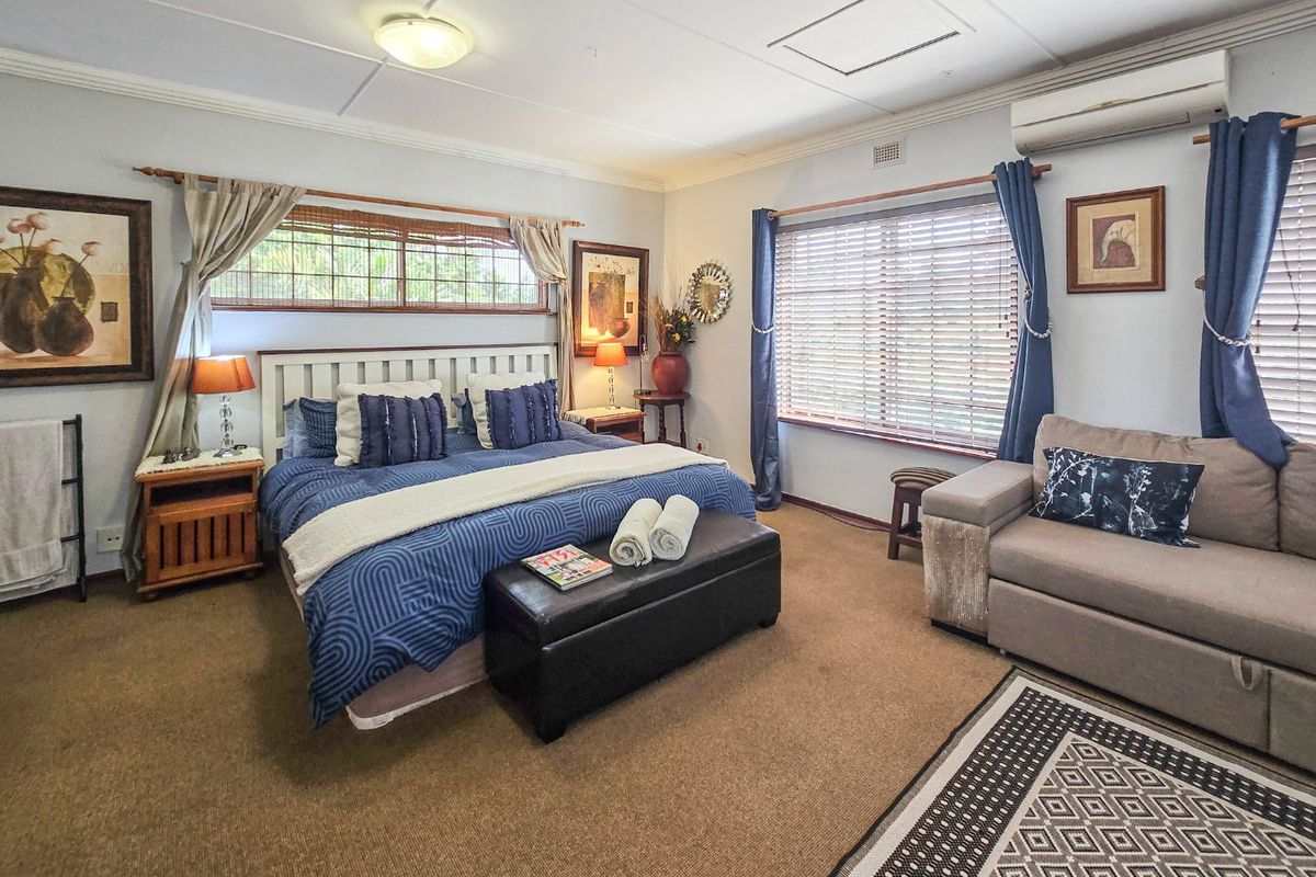 Spacious bedroom featuring neutral wall tones, carpeted flooring, timber blinds, and a wall-mounted split-system air conditioning unit.
