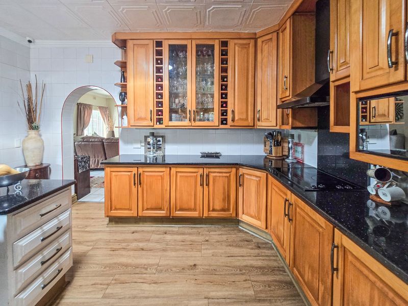 A functional kitchen featuring warm wooden cabinetry, black granite countertops, integrated hob with extractor, and a classic coffered ceiling design.