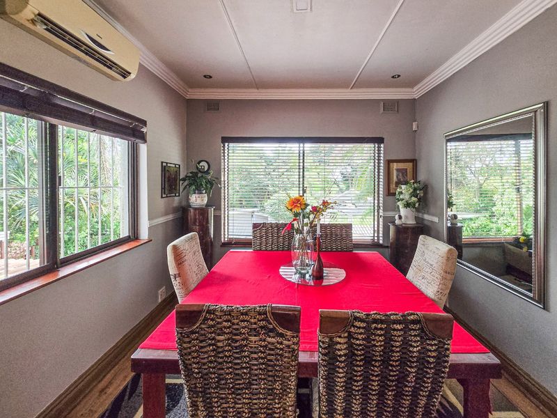A well-maintained dining room featuring crown molding, recessed downlights, and a wall-mounted split-system air conditioner, with large windows providing natural light and garden views.