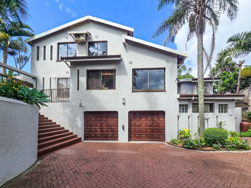 A multi-level residential facade featuring a double garage, paved driveway, and an external staircase leading to an upper-level balcony.