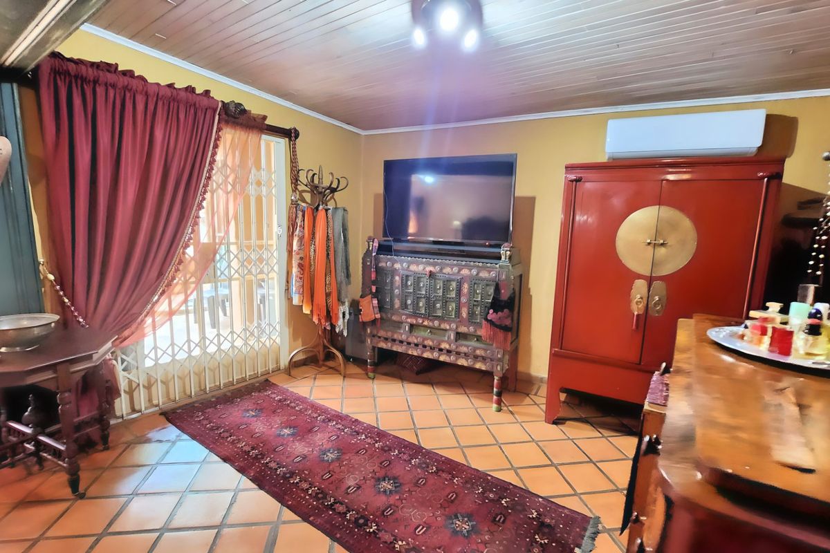 A living room featuring terracotta floor tiles, a timber-paneled ceiling, and a wall-mounted split-system air conditioner with access to an outdoor area via a security gate.