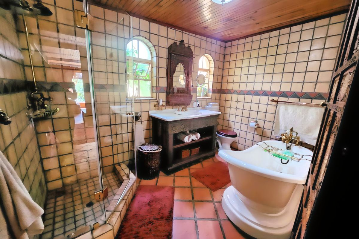 A characterful bathroom featuring a freestanding bathtub, glass-enclosed shower, vanity unit, and traditional terracotta flooring with timber ceiling accents.