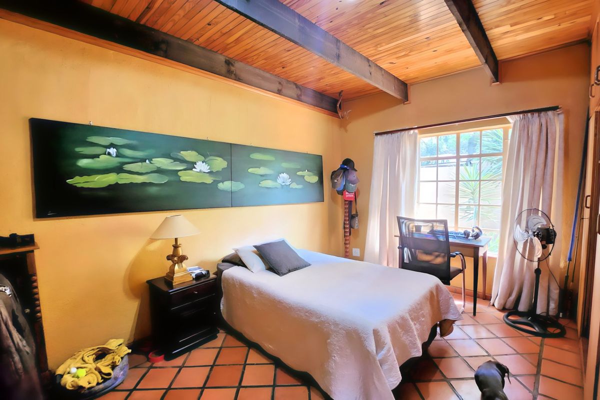 A bedroom featuring exposed timber ceiling beams, terracotta floor tiles, and built-in storage cupboards, offering a warm and rustic aesthetic.