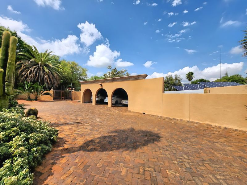 A spacious brick-paved driveway leading to a triple-arched carport, featuring solar panels mounted on the perimeter wall.