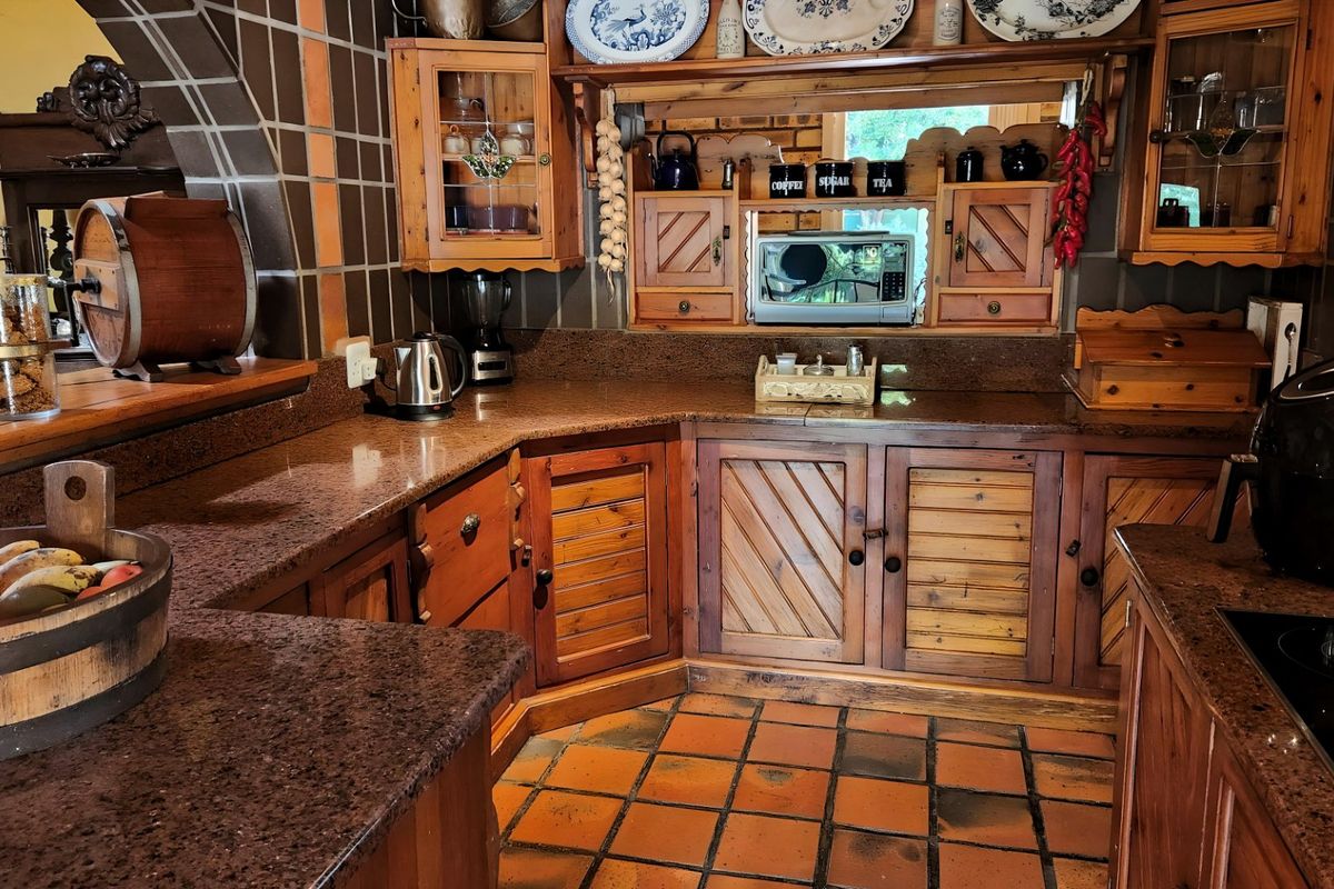 A rustic-style kitchen featuring dark granite countertops, custom wooden cabinetry, and traditional terracotta floor tiles with a built-in microwave and cooktop.