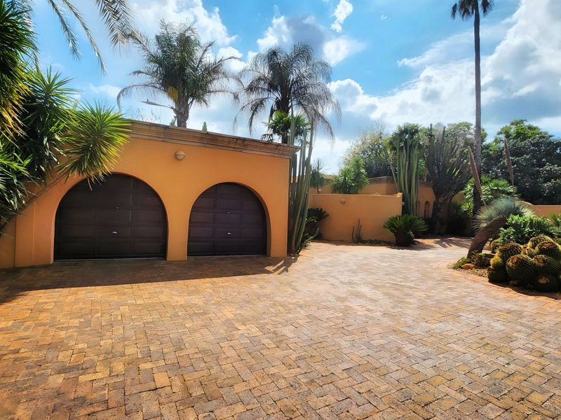 A well-maintained front exterior featuring a double garage with arched entrances and a spacious paved driveway surrounded by established landscaping.