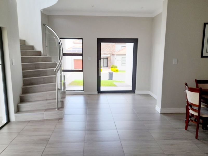 Spacious entrance hall featuring modern tiled flooring, a striking curved staircase with a glass balustrade, and ample natural light through the large glass entrance door.