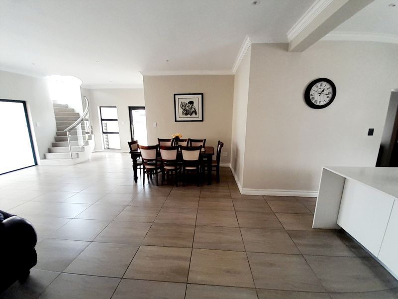 Spacious open-plan living area featuring large format floor tiles, a striking curved staircase, and a modern kitchen island with integrated cabinetry.