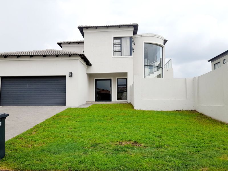 Modern double-story home featuring a sleek white facade, curved glass architectural detail, paved driveway, and an integrated double garage.