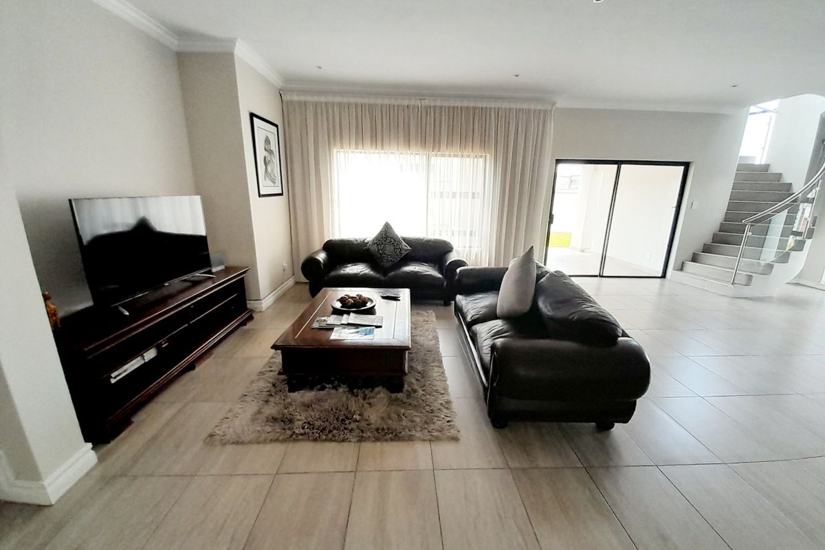 Spacious living room featuring neutral tiled flooring, recessed lighting, and a modern staircase with a metal balustrade, leading to an outdoor patio area.