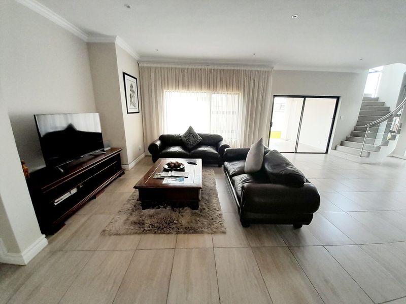 Spacious living room featuring neutral tiled flooring, recessed lighting, and a modern staircase with a metal balustrade, leading to an outdoor patio area.