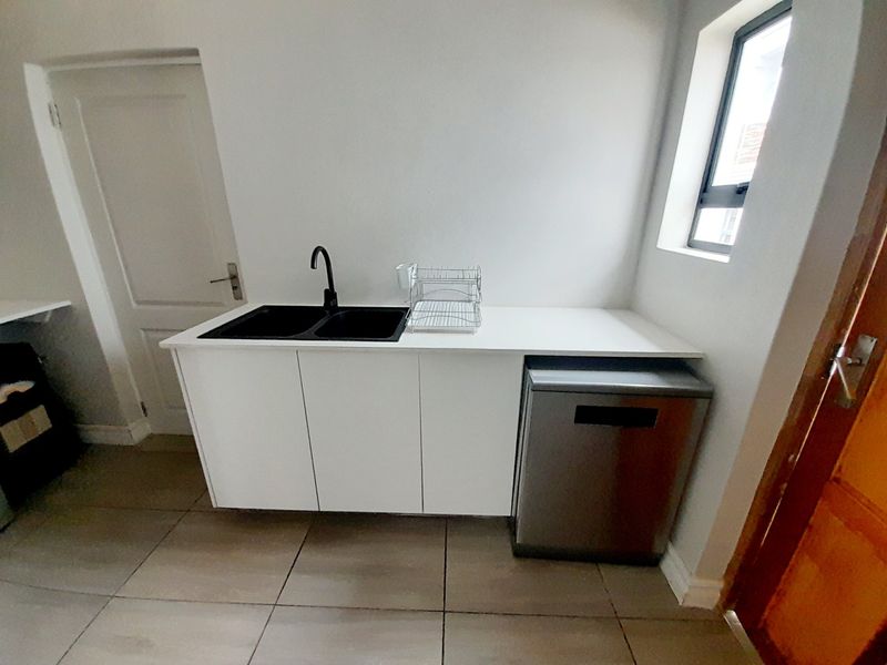A clean and functional scullery area featuring white cabinetry, a double basin sink with a modern black tap, and space for a dishwasher.