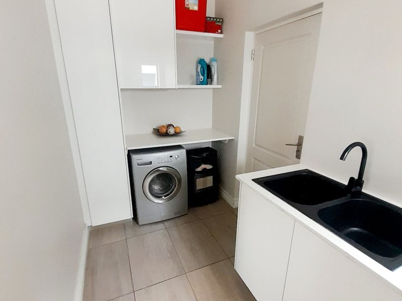 A clean and functional laundry room featuring modern white cabinetry, a double basin sink with a black mixer tap, and neutral tiled flooring.